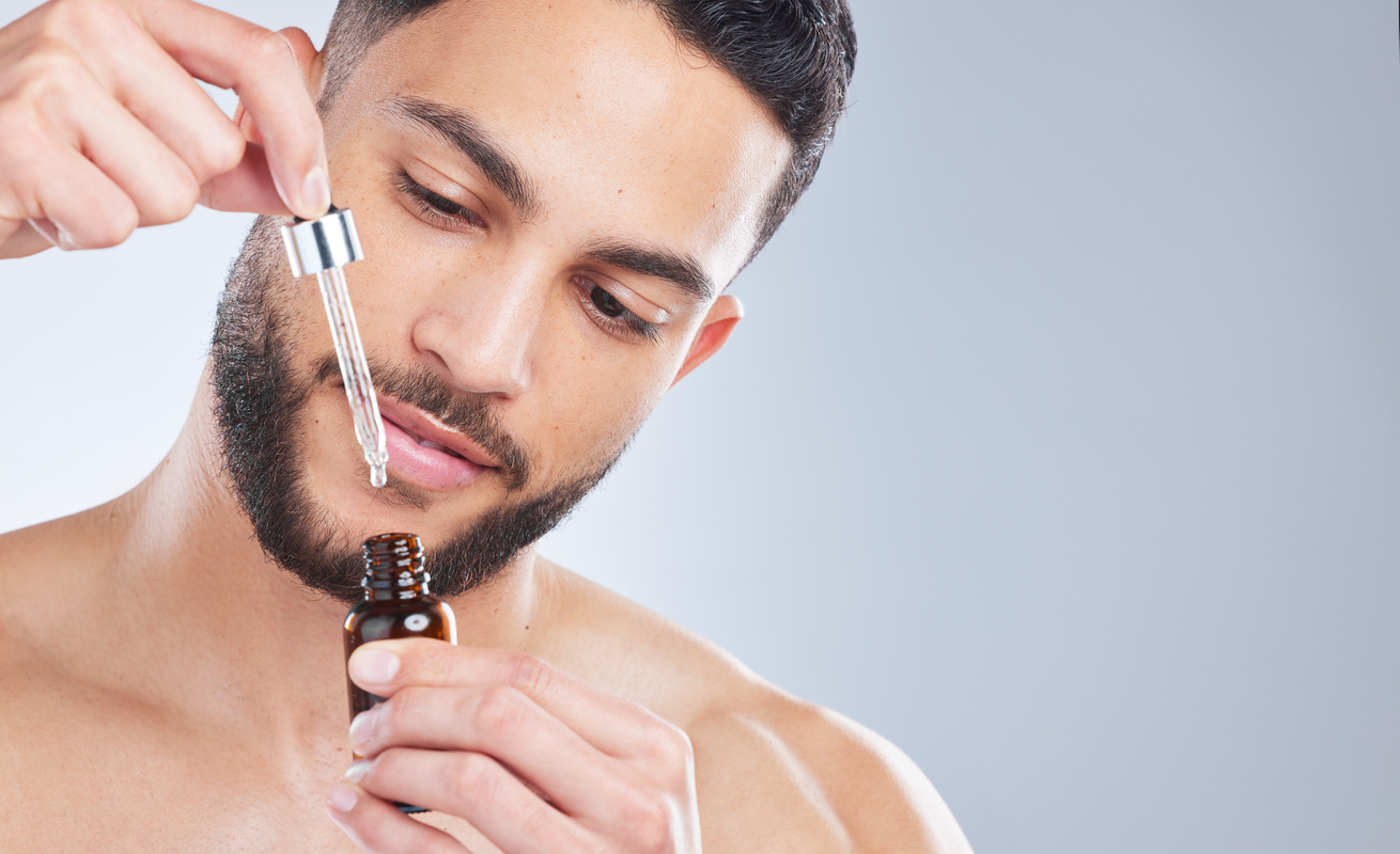 Studio shot of a handsome young man applying serum to his face against a grey background Let's give this bad boy a try
